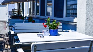 Outdoor seating with tables and benches, a potted plant, and a sign above a window. - Hotel Blauer Karpfen (Oberschleissheim)