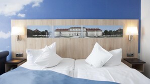 A hotel room with a large bed, two bedside tables with lamps, and a wall-mounted picture of a building. - Hotel Blauer Karpfen (Oberschleissheim)