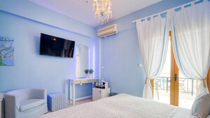 Ein Schlafzimmer mit einem großen Bett, einem an der Wand montierten Fernseher, einem Schreibtisch mit Stuhl und einem Fenster mit Vorhängen.