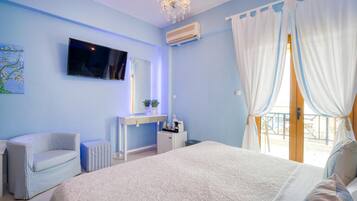 A bedroom with a large bed, a TV mounted on the wall, a desk with a chair, and a window with curtains.