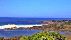A coastal landscape with a beach, vegetation, and a distant building. - Pazo do Souto (Carballo)