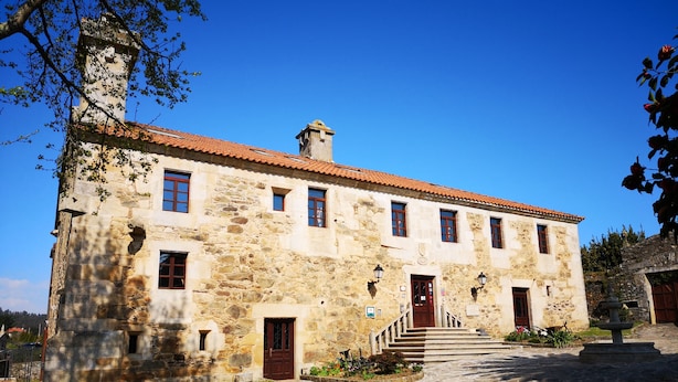 A stone building with a red-tiled roof, multiple windows, and a central staircase leading to a door. - Pazo do Souto (Carballo)