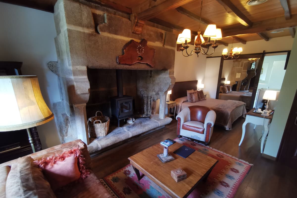 Una habitación acogedora con chimenea de piedra, sofá de madera, sillón de cuero y una mesa de centro con libros y una lámpara.