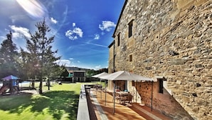 A stone building with a patio area featuring outdoor seating and a play structure in the background. - Pazo do Souto (Carballo)