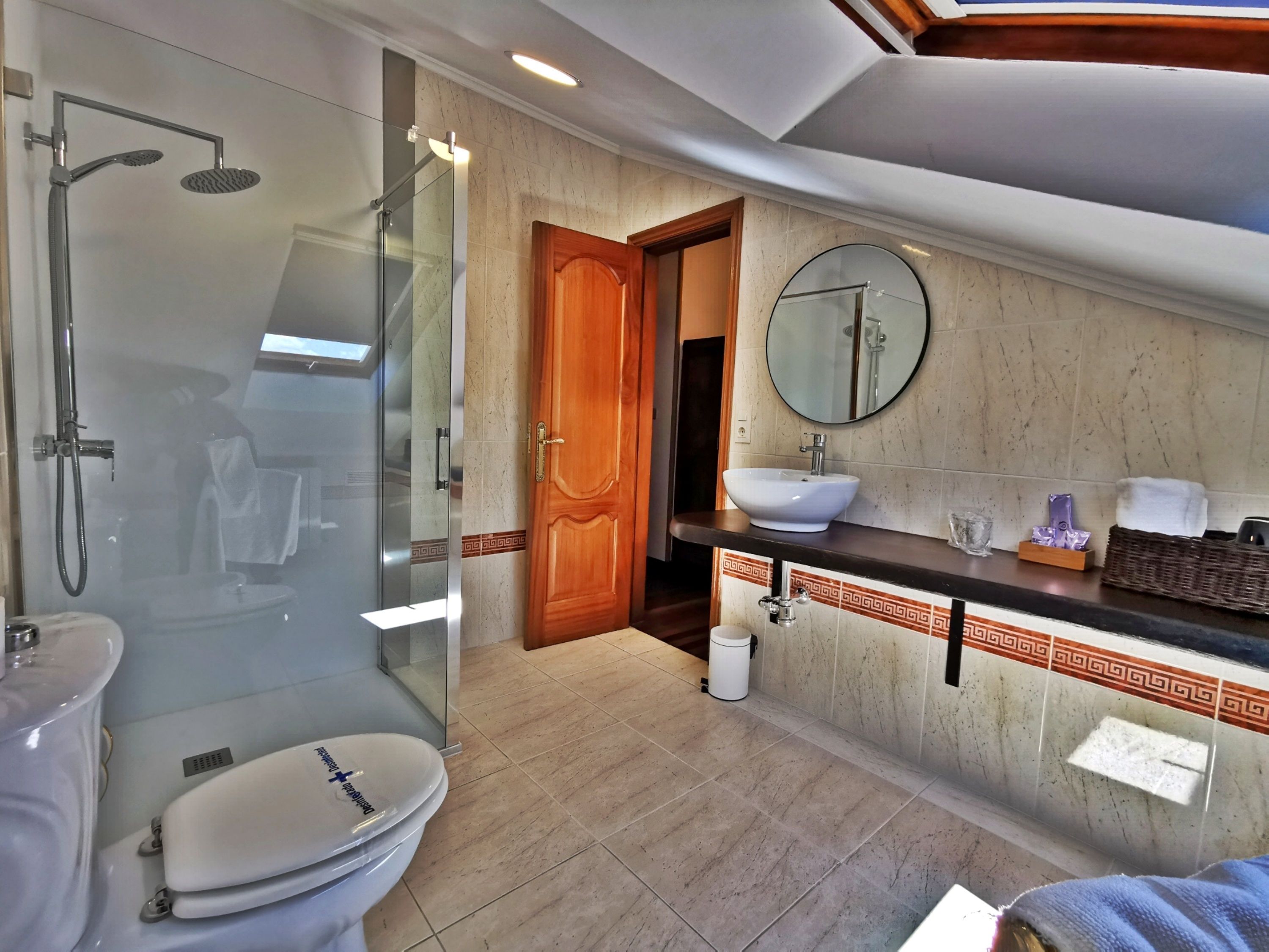 A modern bathroom with a glass-enclosed shower, a white toilet, a sink with a mirror above it, and a wooden door.