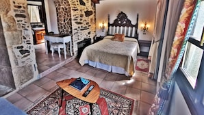 A bedroom with a stone wall, a wooden ceiling, a bed with a headboard, a desk, and a chair. - Pazo do Souto (Carballo)