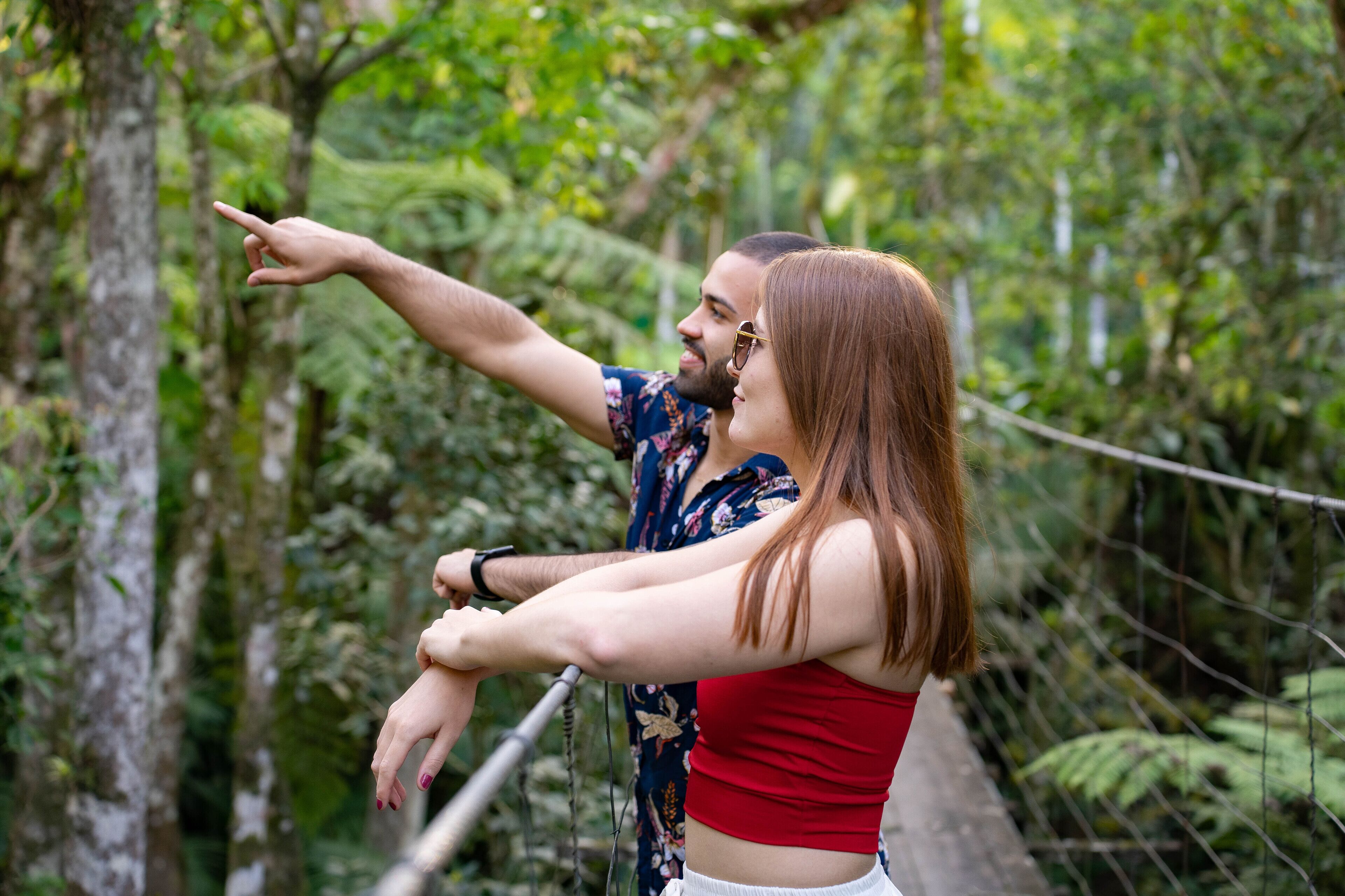 A couple on a suspension bridge surrounded by lush greenery.