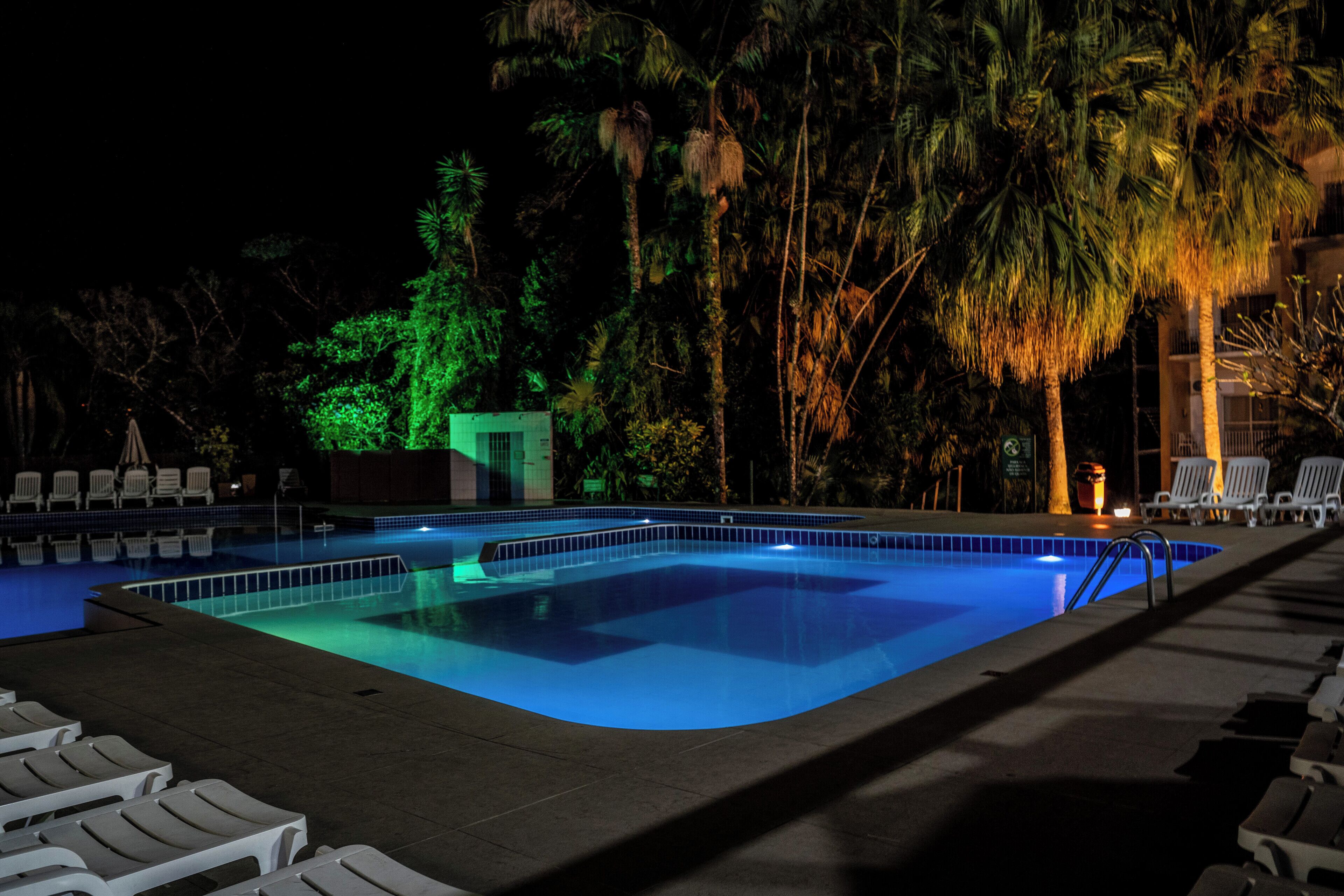 Una piscina con sillones de descanso y palmeras de noche.