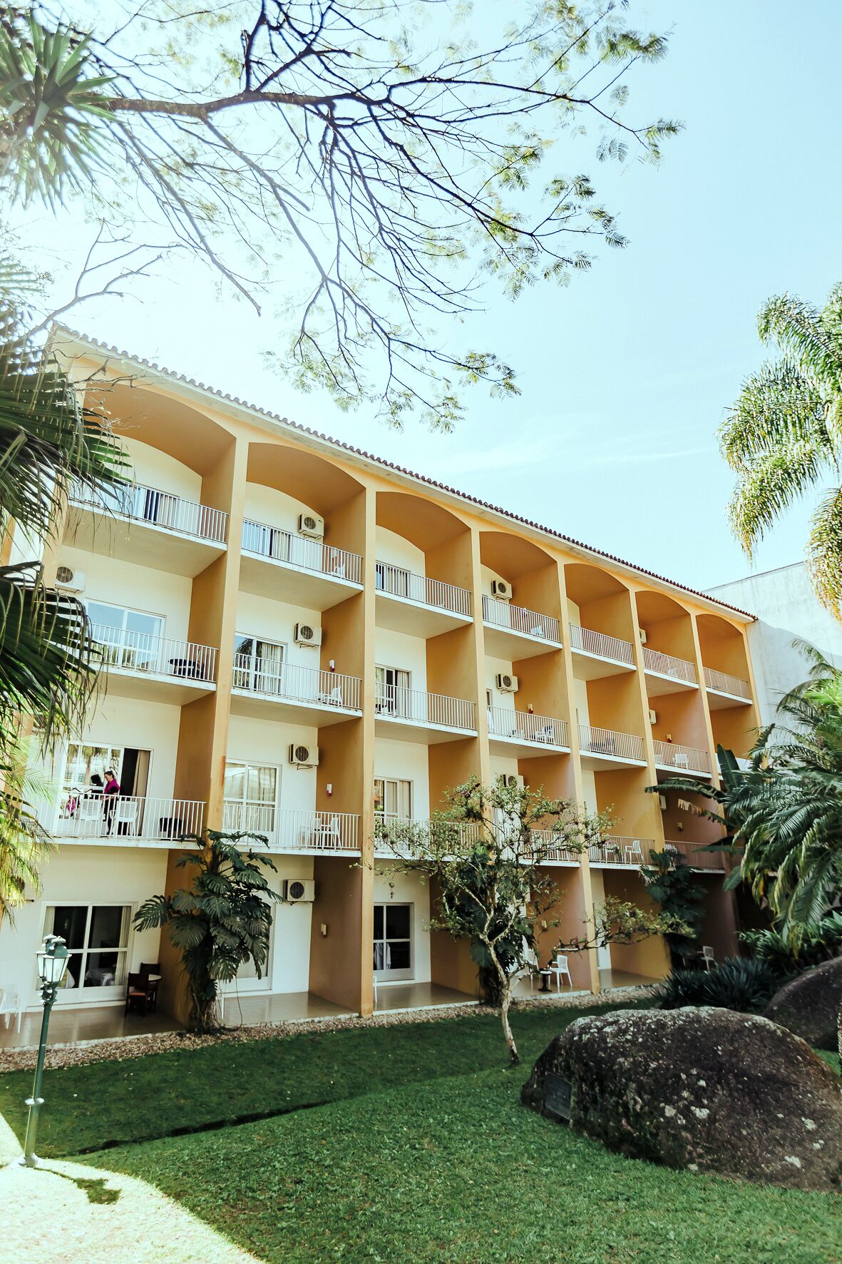 A multi-story hotel with balconies, a well-maintained lawn, and surrounding greenery.
