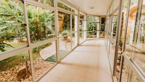 A corridor with glass walls and a tiled floor, leading to a spa area with a pool and greenery.