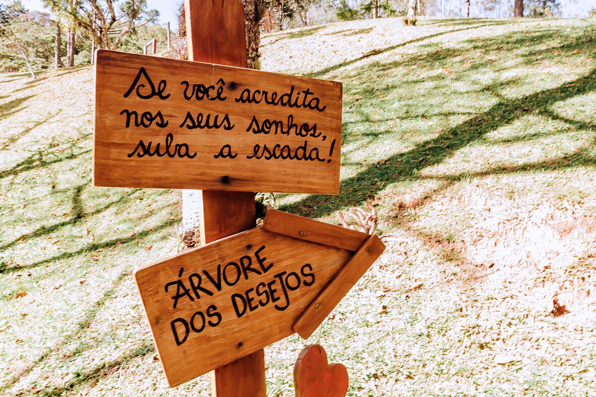 Un cartel de madera con texto en portugués, que indica una dirección hacia 'ÁRVORE DOS DESEJOS'.