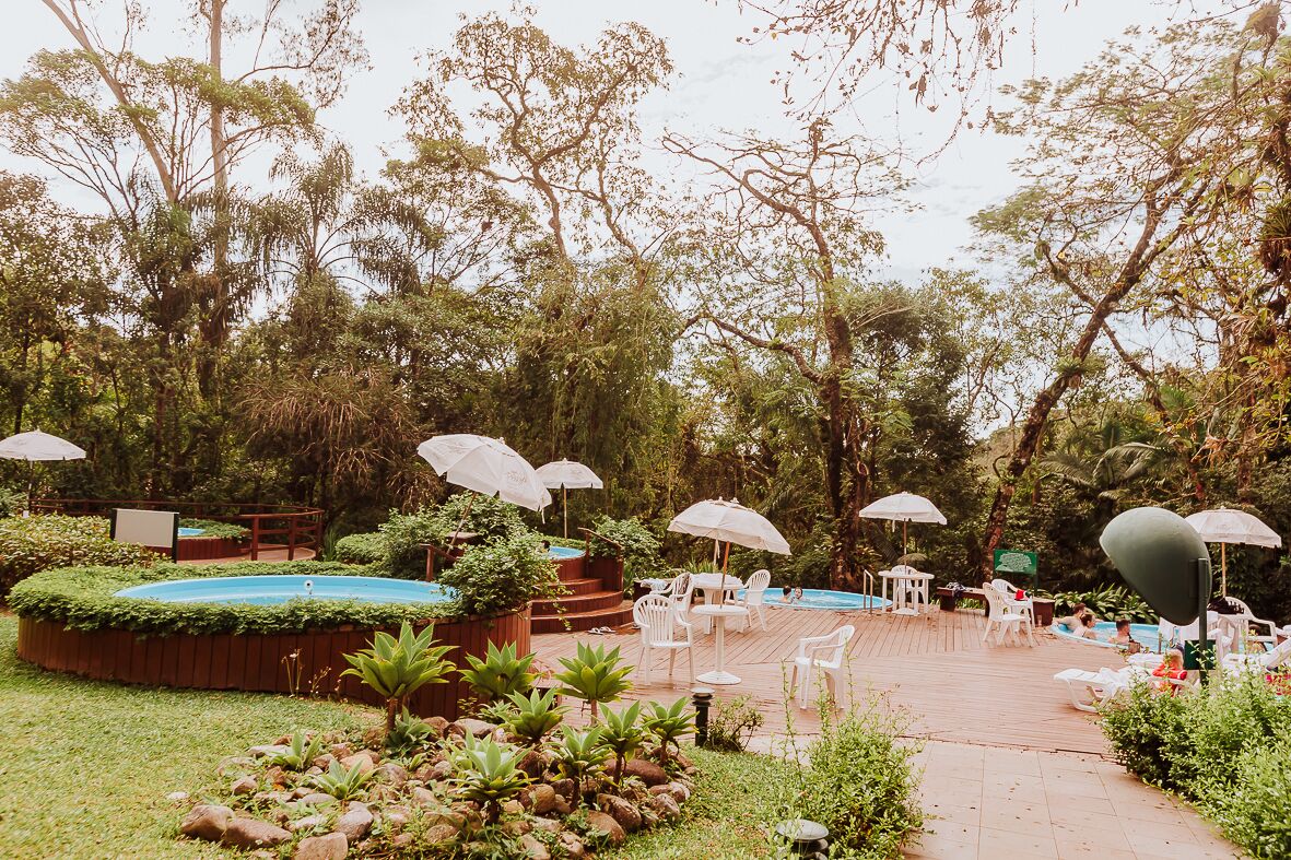 An outdoor garden with a pool, surrounded by lush greenery and white umbrellas.