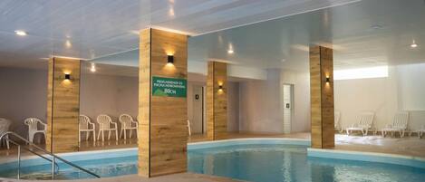 An indoor swimming pool with wooden pillars, white chairs, and a sign indicating the depth of the pool.