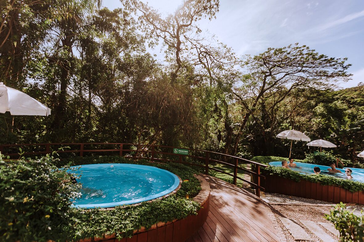 A swimming pool area with a wooden deck, surrounded by lush greenery and trees.