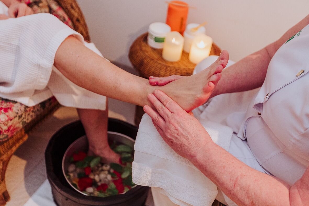 Fußmassage mit Fußbad und Kerzen im Hintergrund.