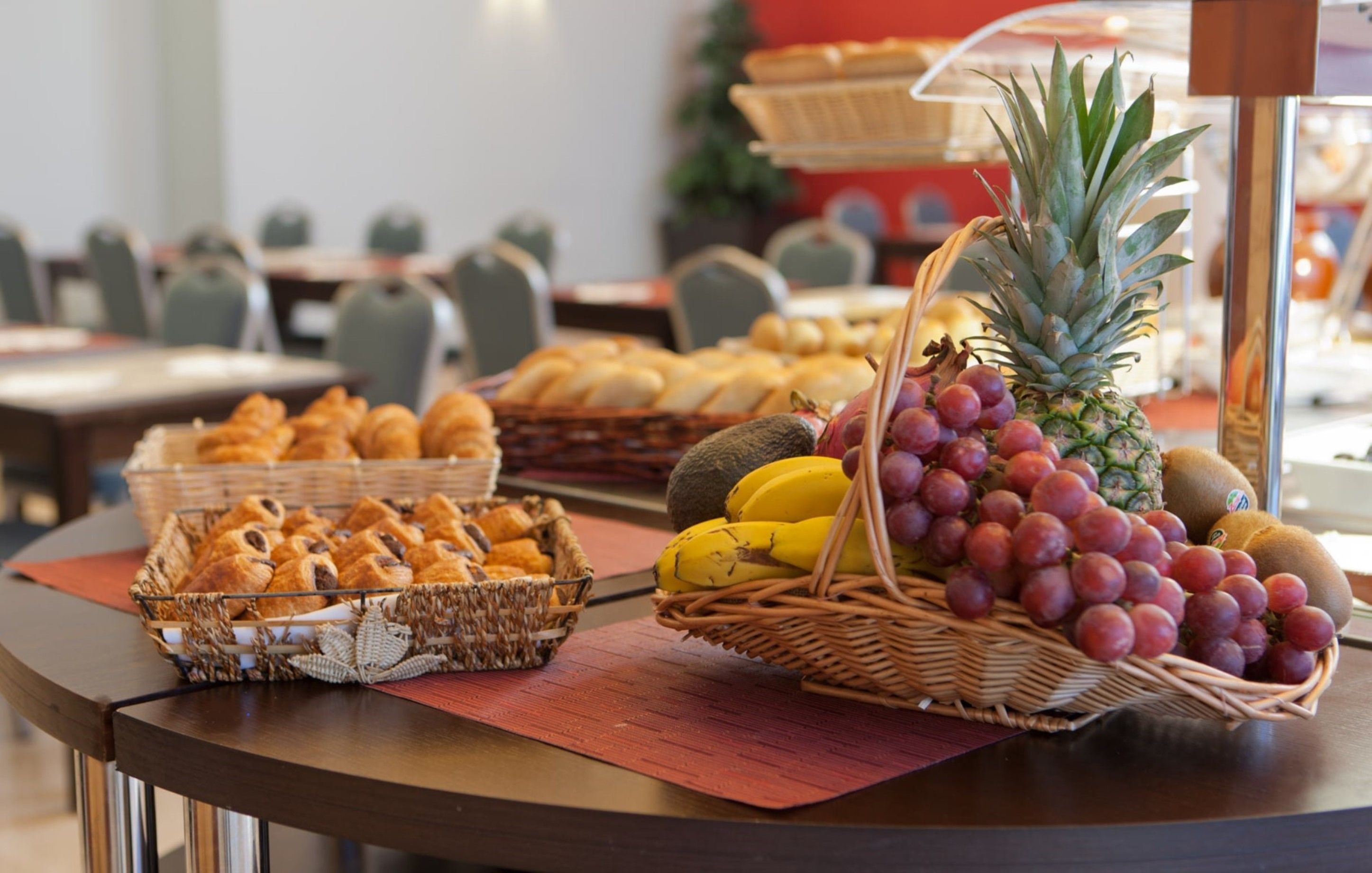 Une table de buffet proposant divers aliments, notamment du pain, des fruits et des pâtisseries.