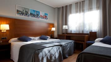 Ett hotellrum med två sängar, ett skrivbord och en stol. Det finns två lampor på nattborden, en tv som är monterad på väggen och ett stort fönster med gardiner.