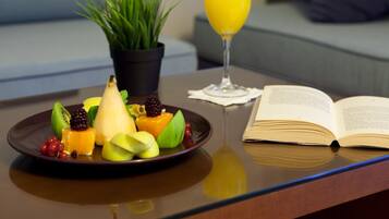 Una mesa de comedor con un plato de fruta, un vaso de zumo de naranja, un libro y una planta en maceta.