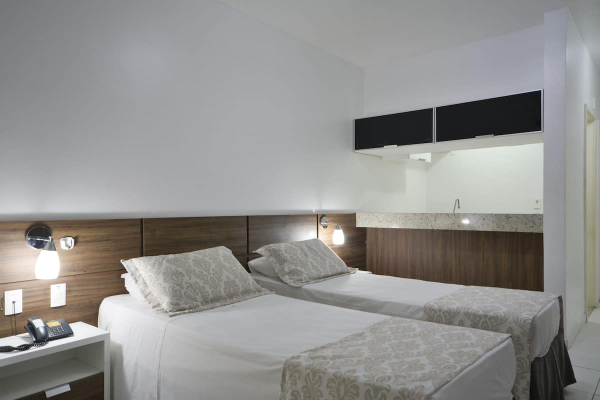 Ein Hotelzimmer mit zwei Betten, einem Schreibtisch mit Telefon und einem an der Wand befestigten Fernseher.