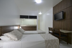 A hotel room with two beds, a desk, a chair, a TV, and a bathroom with a mirror and sink.