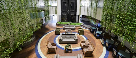 A spacious indoor atrium with a central seating area, surrounded by tables and chairs, and walls adorned with hanging greenery.