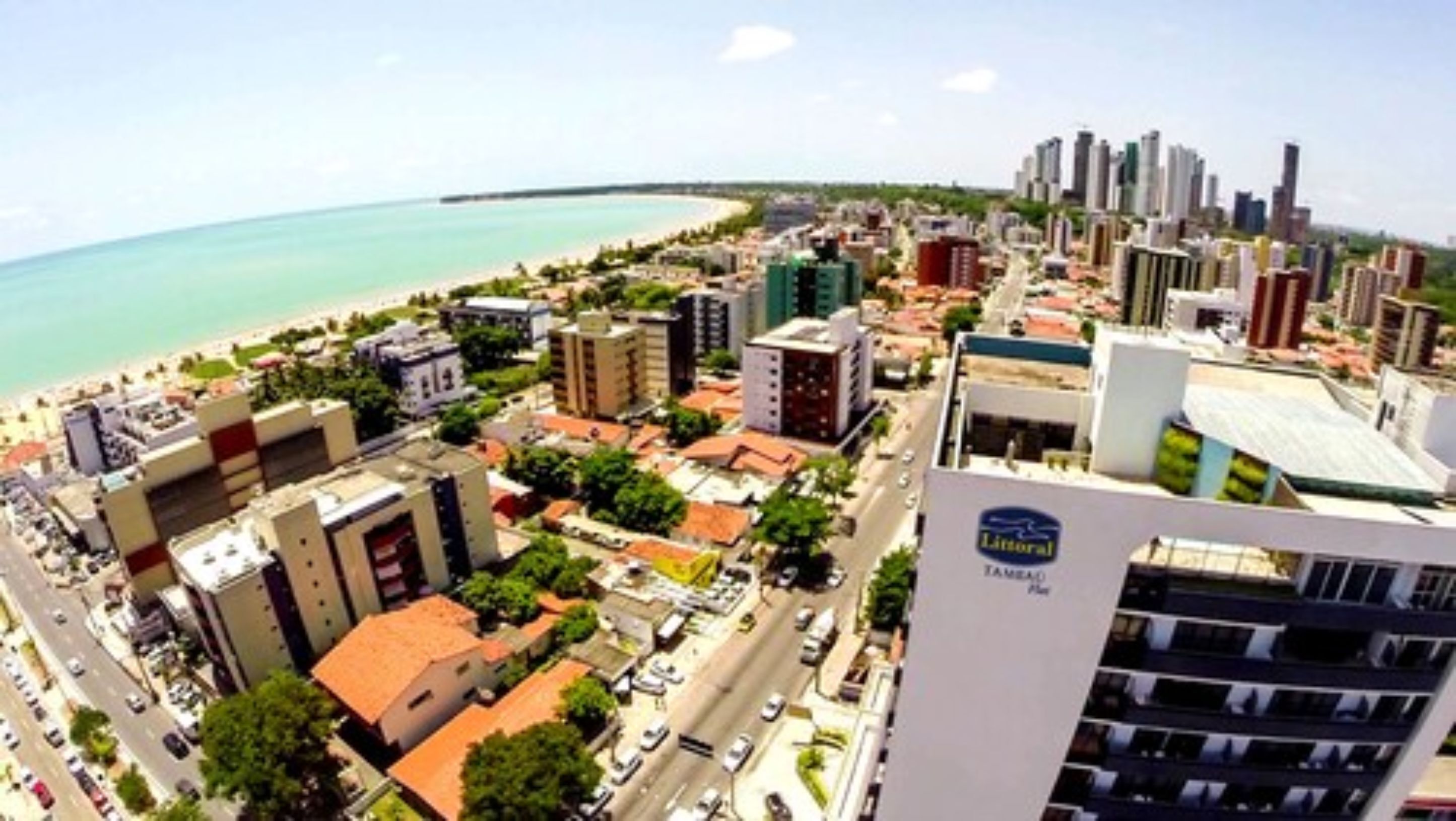 Un paisaje urbano costero con una mezcla de edificios altos y estructuras más pequeñas, una playa y un cielo despejado.