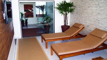 Un solárium con dos sillones de madera, una planta grande en maceta y un ventanal de vidrio que da a un patio.