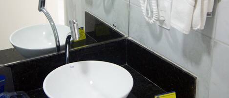 Un baño con un lavabo blanco, un espejo y dos secadores de pelo fijos en la pared.