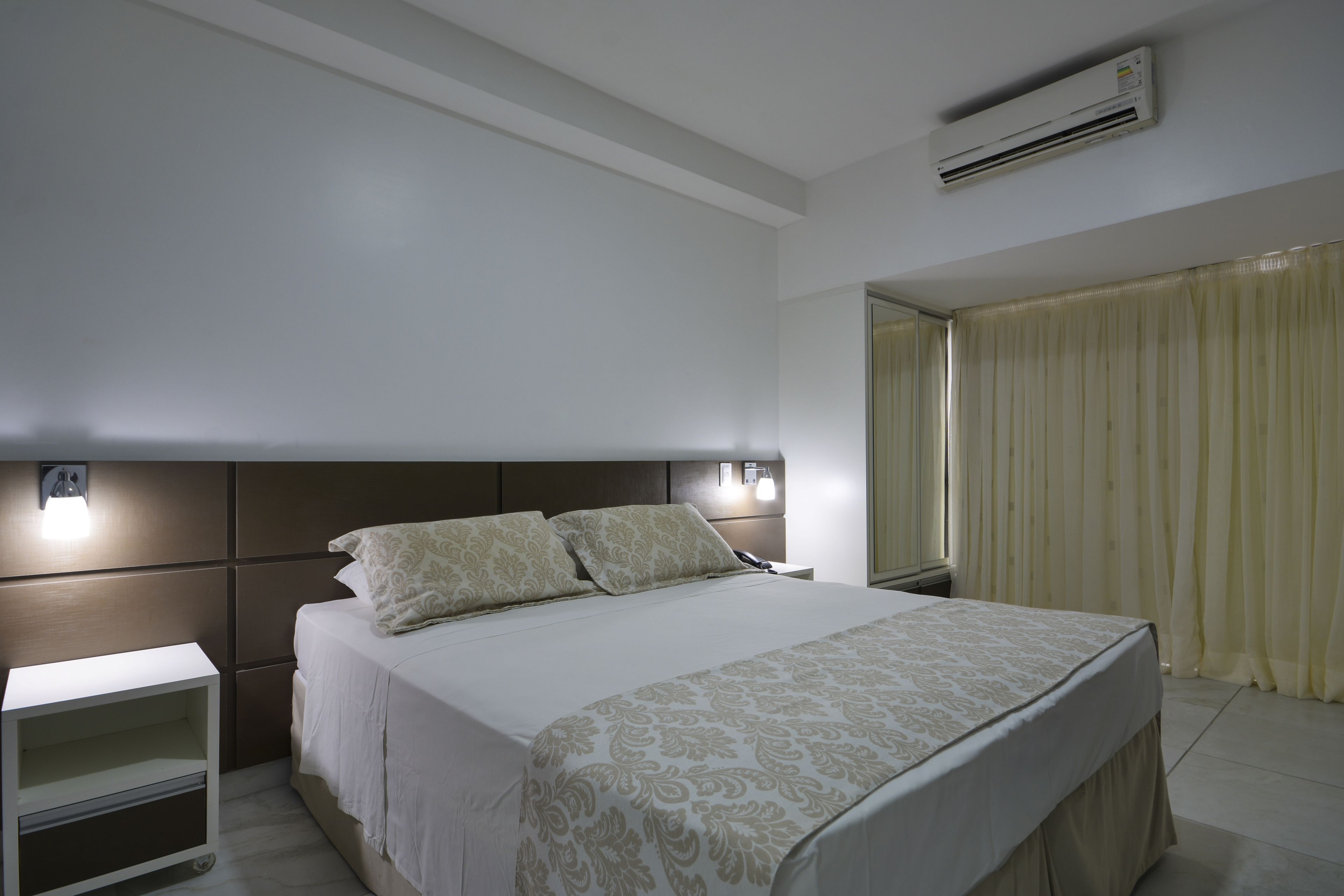 A hotel room with a large bed, bedside lamps, a nightstand, and a window with curtains.