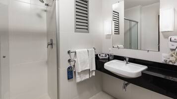 Un baño moderno con cabina de ducha de vidrio, un lavamanos blanco y un espejo grande.