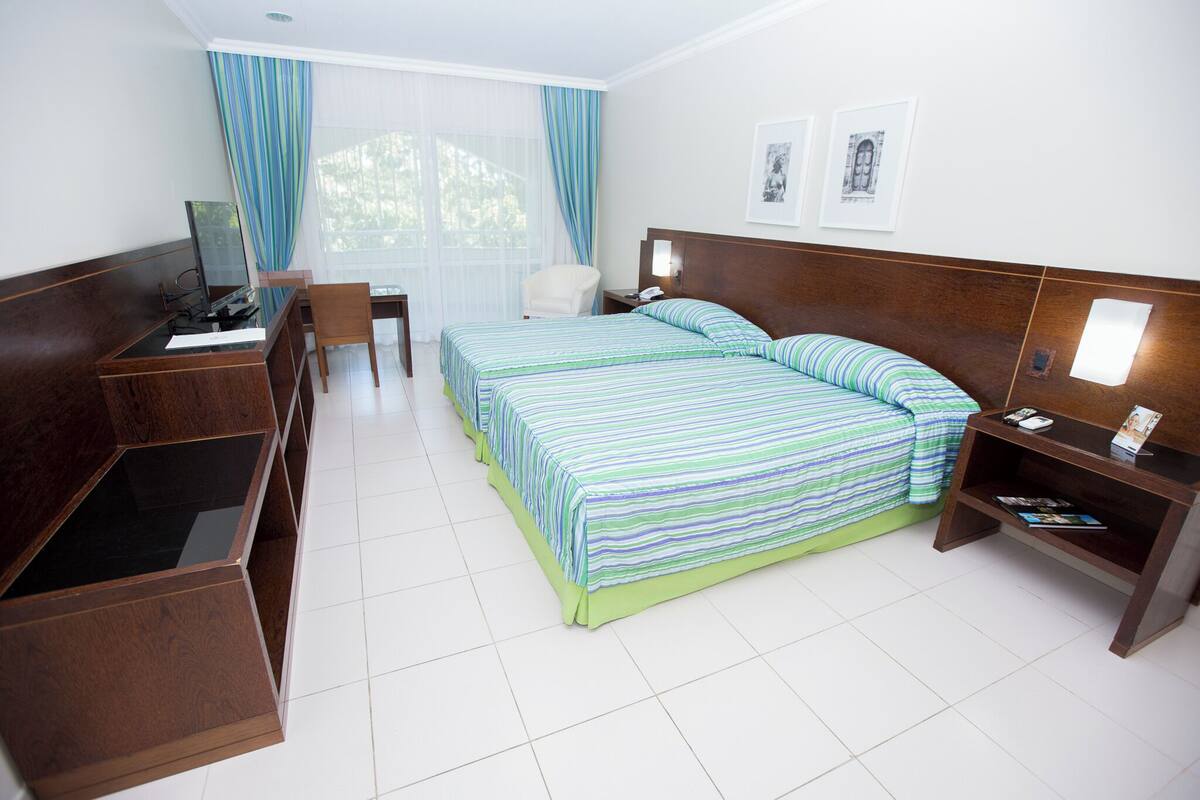 Habitación de hotel con cama, escritorio, silla, mesita de noche y ventana con cortinas.
