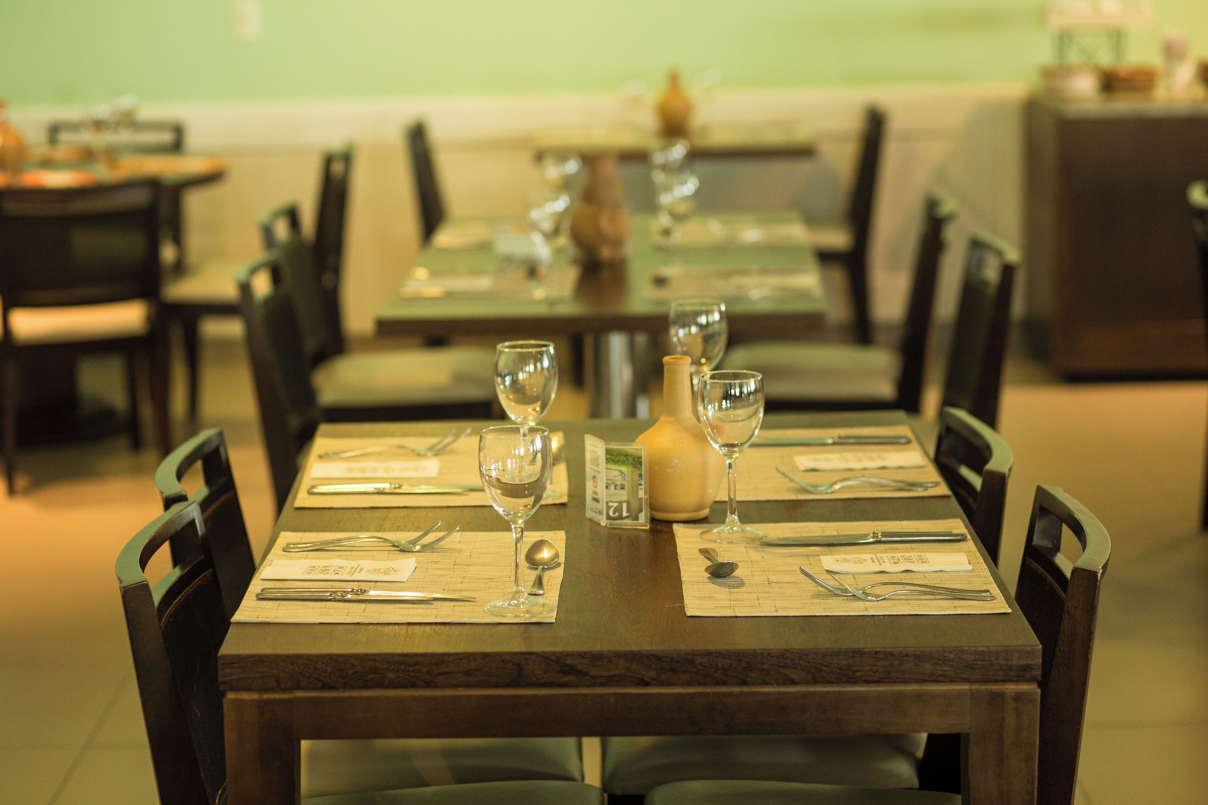 Un comedor de restaurante con mesas dispuestas para dos, cada una con cubiertos, vasos y una carta.