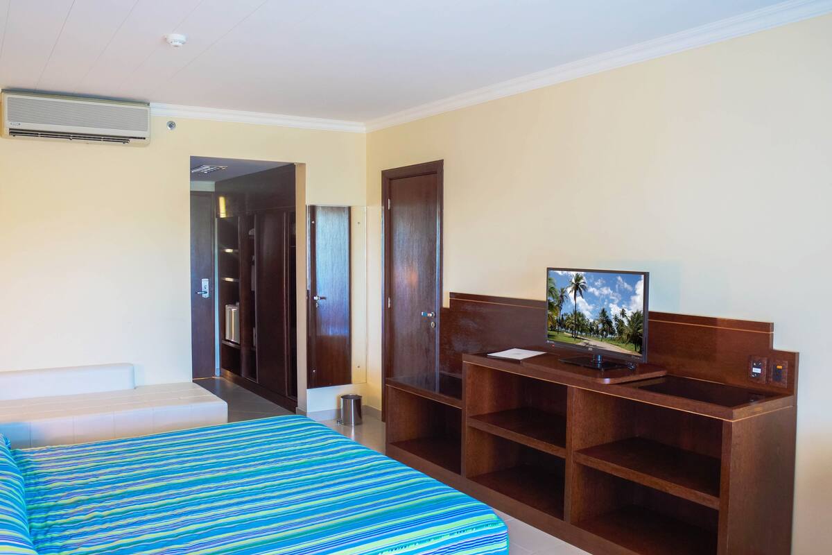 Habitación de hotel con cama, escritorio con computadora, televisor y puerta que da a otra habitación.