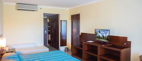 A hotel room with a bed, a desk with a computer, a television, and a door leading to another room.