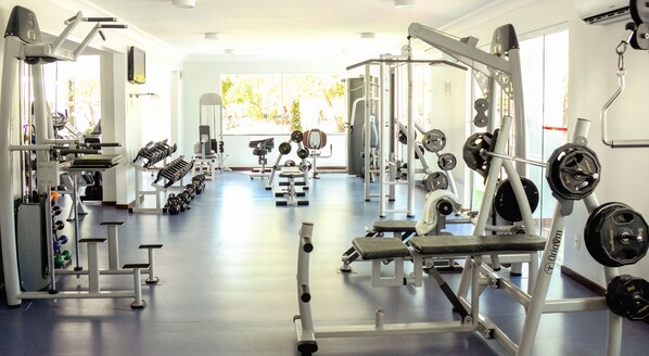 Een fitnessruimte met diverse trainingsapparaten, waaronder gewichten, krachtapparaten en banken.