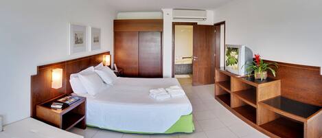 A hotel room with a bed, bedside table, nightstand, and a wooden console table with a plant.