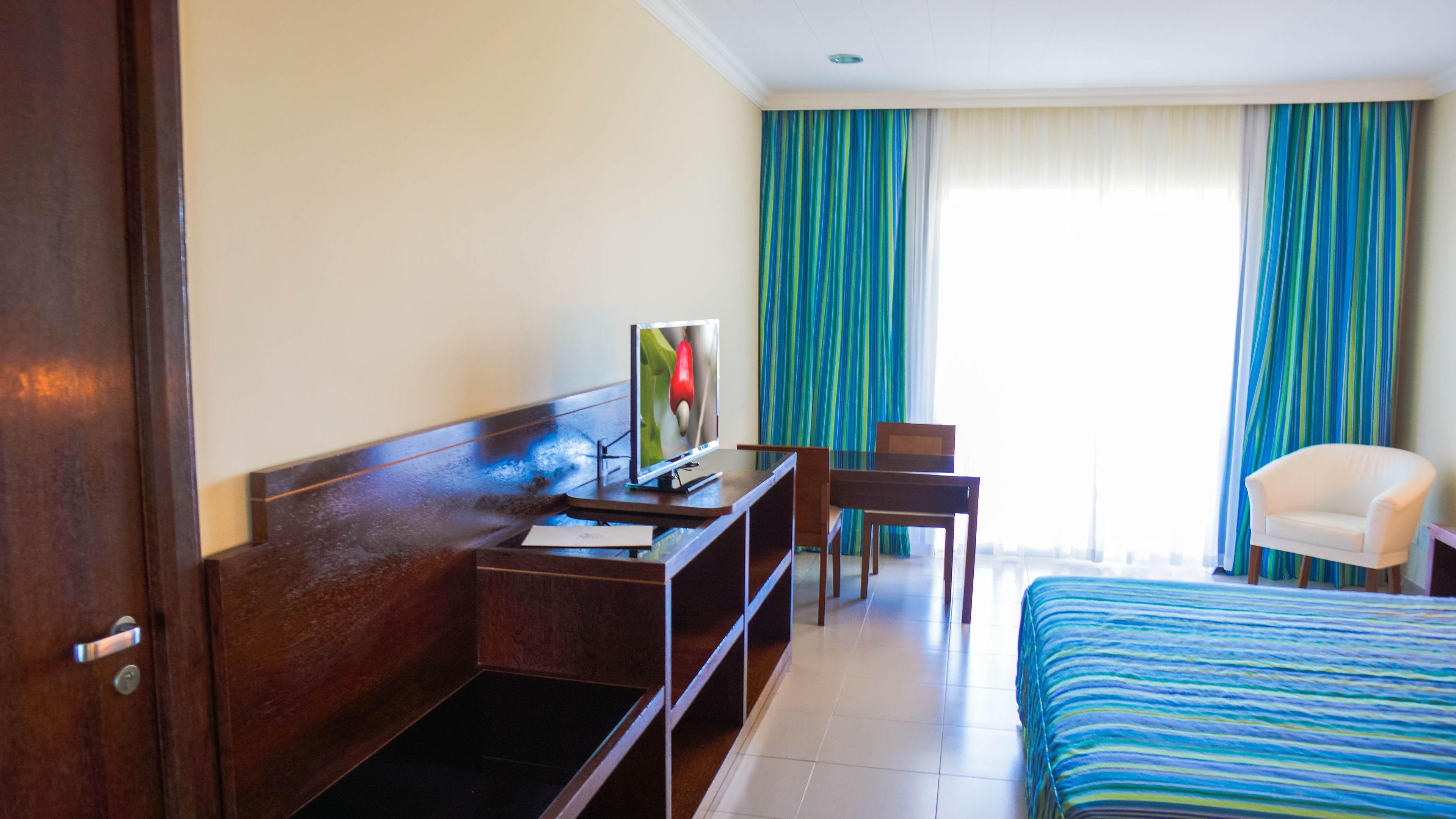 A hotel room with a bed, a desk with a computer, a chair, and a TV.