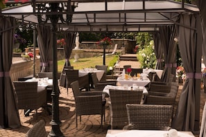 An outdoor patio with wicker furniture, white tablecloths, and a stone floor. - Schlosshotel Zum Markgrafen (Quedlinburg)