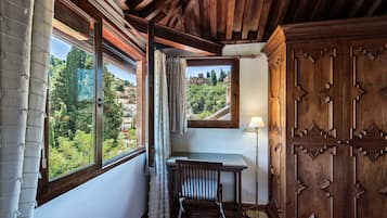 A room with a wooden ceiling, a desk with a chair, a window with curtains, and a lamp.