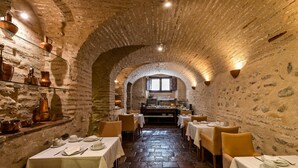 A narrow, stone-walled dining area with tables set for meals, a kitchen in the background, and rustic decor. - Casa Morisca Hotel Boutique (Granada)