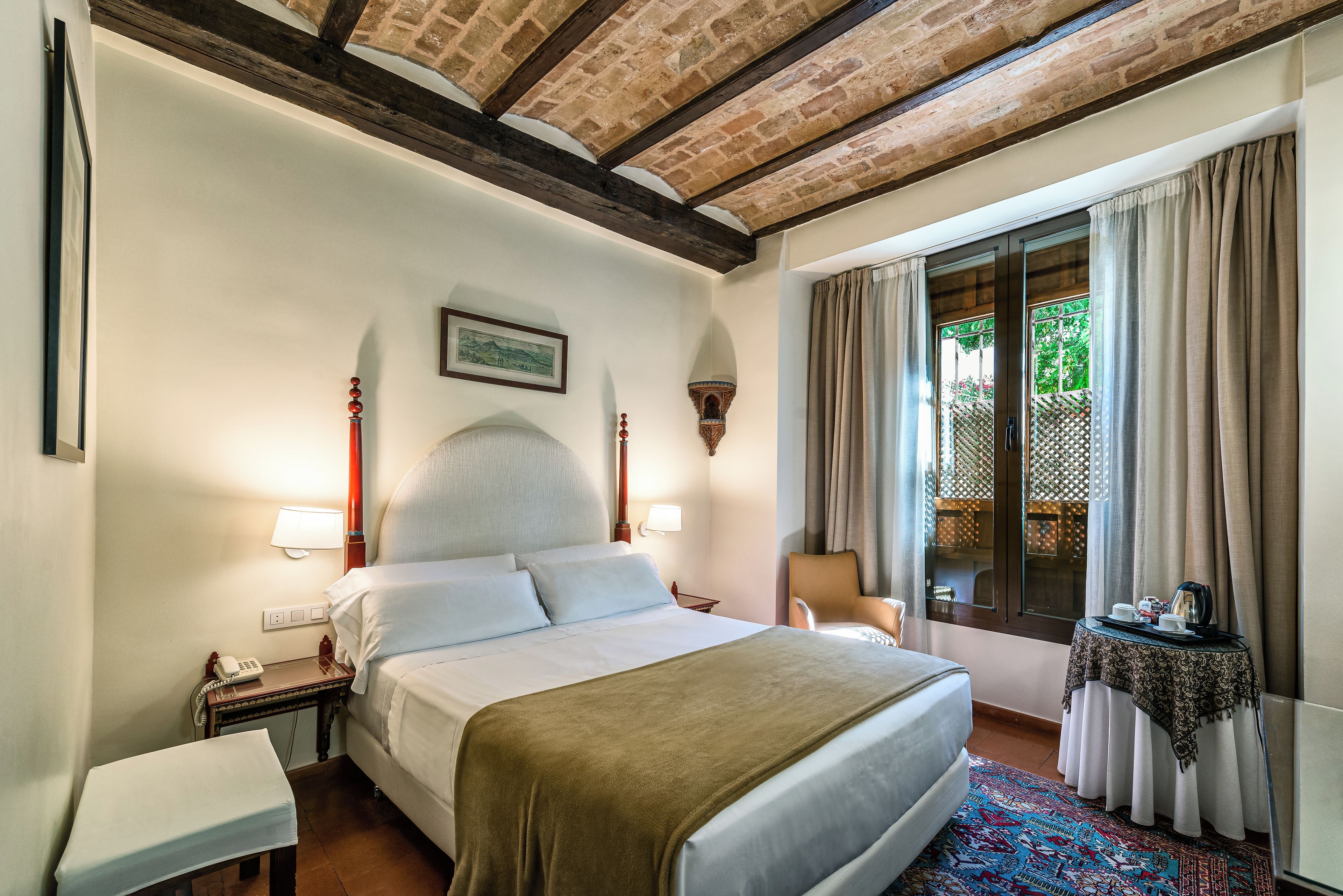 A hotel room with a bed, bedside table, lamp, and a window with curtains.