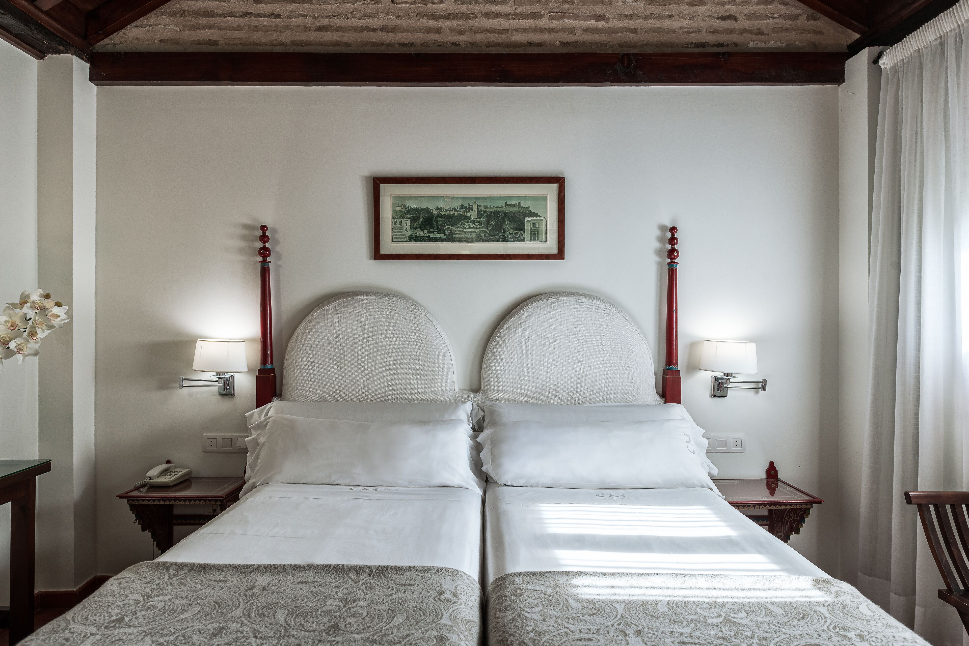 A double bed with a headboard, two bedside tables, a framed picture on the wall, and a window with curtains.