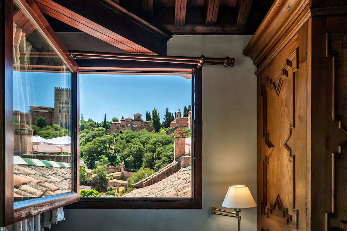 A room with a large window offering a view of a historic town with buildings and trees.