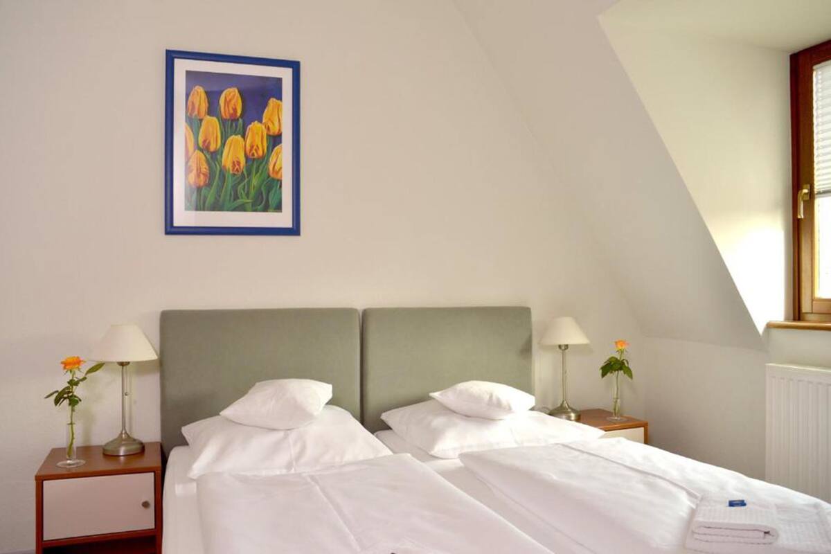 A hotel room with two beds, white linens, a framed painting of yellow tulips, and a window with blinds.
