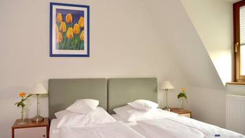 A hotel room with two beds, white linens, a framed painting of yellow tulips, and a window with blinds.