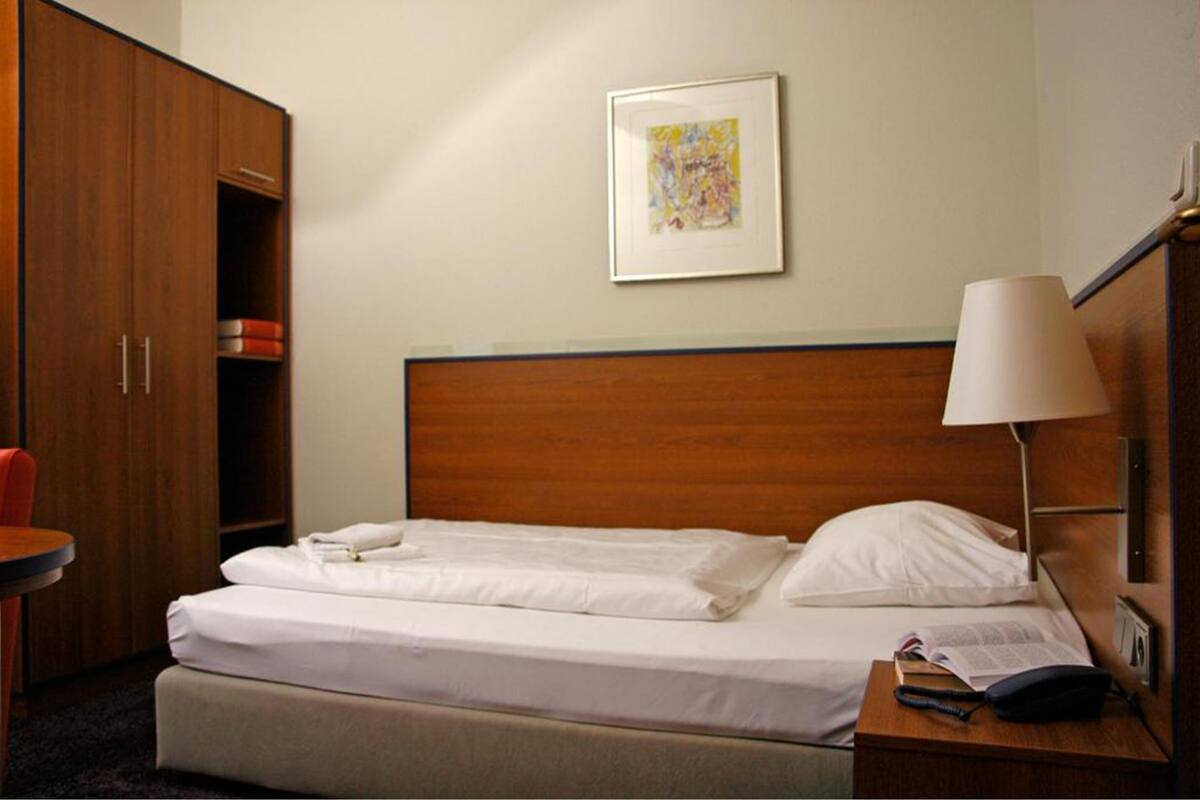 A hotel room with a bed, a nightstand, a lamp, a wardrobe, and a framed picture on the wall.