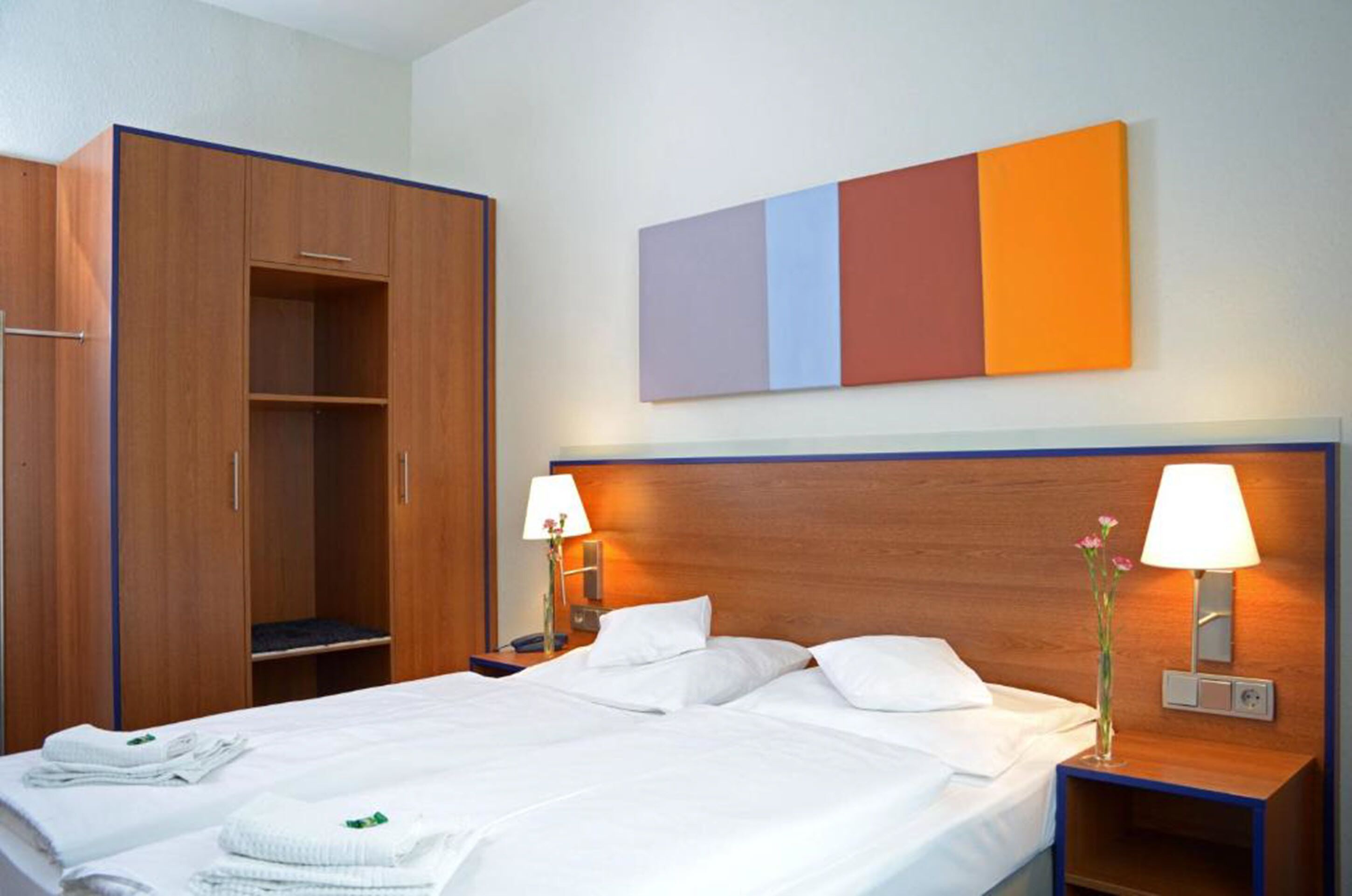 Ein Hotelzimmer mit einem Bett, zwei Nachttischen, einem Kleiderschrank und einem Wandbild.