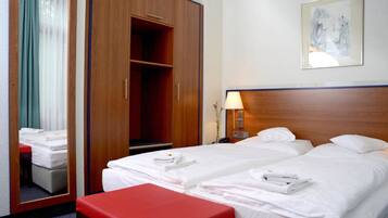 Habitación de hotel con dos camas, un armario de madera, un banco rojo, una mesita de noche con lámpara y un cuadro enmarcado en la pared.