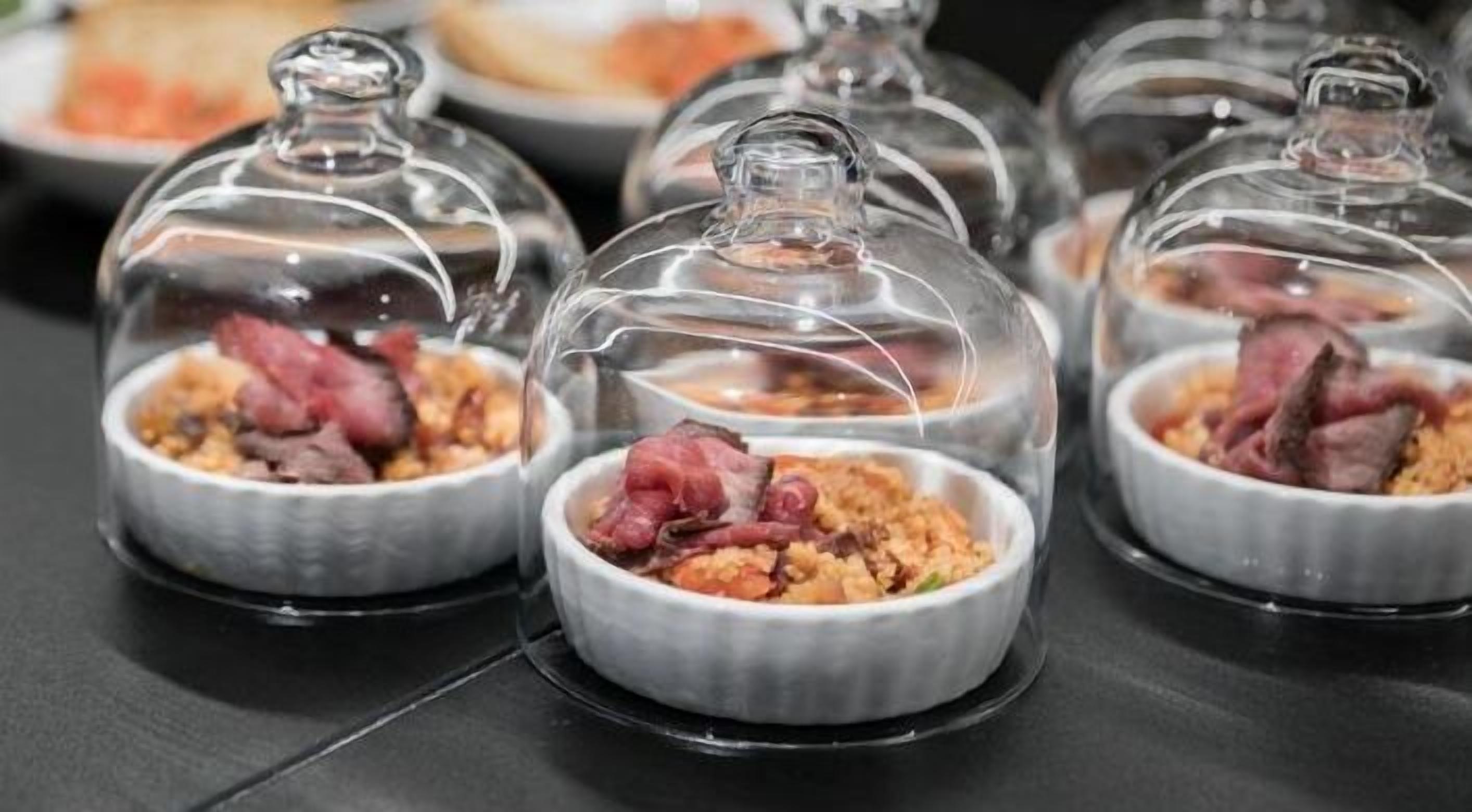 Una mesa con varios domos de cristal que cubren platos con carne y verduras.