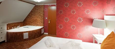Een hotelkamer met een bed, een badkamer met een bad, en bloemenbehang in het rood.